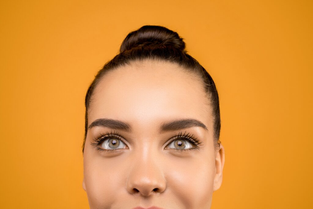 Detailed close-up of a woman's face against a vibrant orange background, showcasing expressive eyes.